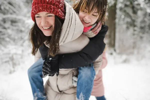 Cute teen girl and her mother having fun on a walk in snow covered pine forest on chilly winter day. Teenage child exploring nature. Winter activities for kids.