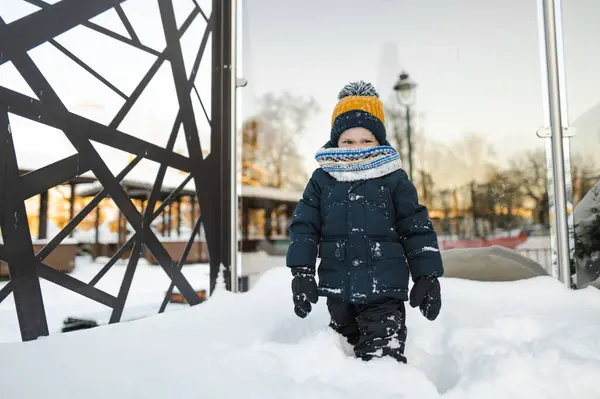 雪の降る冬の日に街で楽しんでいる愛らしい幼児の少年 雪の中で遊ぶ暖かい服を着ているかわいい子供 子供と家族のための冬の活動 — ストック写真