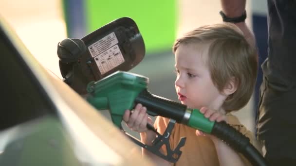 かわいい金髪の少年がポンプノズルを握り 父親がガソリンスタンドで車を燃やすのを手伝った 小さな子供のヘルパー クローズアップスローモーション映像 — ストック動画