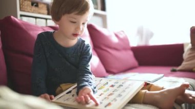 Güneşli bir öğleden sonra evdeki kanepede kitap okuyan tatlı çocuk. Gündüz kreşinde yaratıcı aktivite. Çocuklar eğleniyor. Eğitici öğrenme oyunları. Aile içi eğlence..