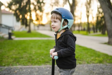 Güneşli bir yaz akşamında güzel bir çocuk mobiletiyle şehirde geziyor. Paten süren küçük bir çocuk. Çocuklar için aktif eğlence ve açık hava sporları.