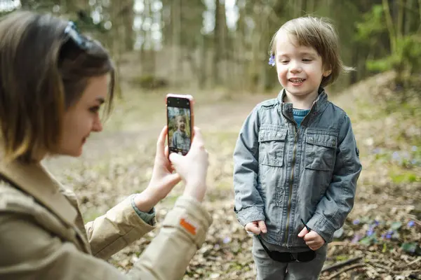Teenage sister taking a photo of her toddler brother. Adorable teen girl hiking in the woods with her little sibling. Children with large age gap. Big age difference between siblings.