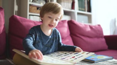 Güneşli bir öğleden sonra evdeki kanepede kitap okuyan tatlı çocuk. Gündüz kreşinde yaratıcı aktivite. Çocuklar eğleniyor. Eğitici öğrenme oyunları. Ev içi aile eğlencesi. Yavaş çekim görüntüleri.