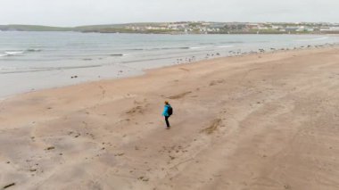 Kilkee sahilinde genç bir bayan turist, küçük bir sahil kasabası, sahil beldesi kadar popüler, at nalı koyunda yer alıyor ve Duggerna Resifi tarafından Atlantik Okyanusu 'ndan korunuyor. Ortak Clare, İrlanda.