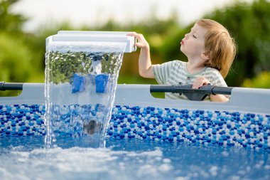 Küçük sevimli çocuk açık havuz kenarında eğleniyor. Çocuk suyla oynuyor. Havuzda aile eğlencesi. Çocuklu aile için yaz etkinlikleri.