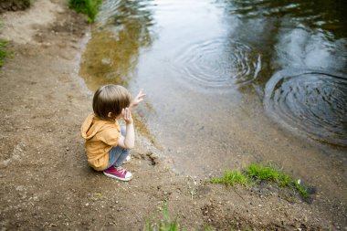 Sıcak yaz gününde gölün ya da nehrin kenarında oynayan tatlı bir çocuk. Sevimli çocuk yaz tatillerinde dışarıda eğleniyor. Çocuklar için su aktiviteleri.