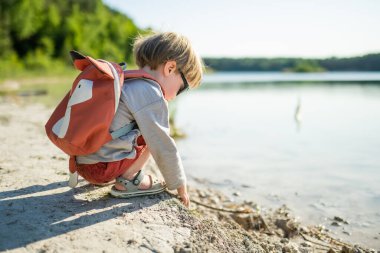 Sıcak yaz gününde gölün ya da nehrin kenarında oynayan tatlı bir çocuk. Sevimli çocuk yaz tatillerinde dışarıda eğleniyor. Çocuklar için su aktiviteleri.