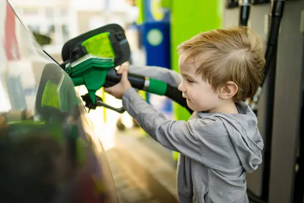 可爱的金发碧眼的小男孩拿着泵喷嘴 一个有趣的小男孩在加油站帮爸爸给汽车加油 爸爸的小助手 — 图库照片