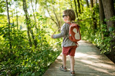 Sırt çantalı şirin bir çocuk güneşli bir yaz gününde dışarıda eğleniyor. Doğayı keşfeden çocuk. Çocuk seyahate çıkıyor. Çocuklu aileler için yaz etkinlikleri.