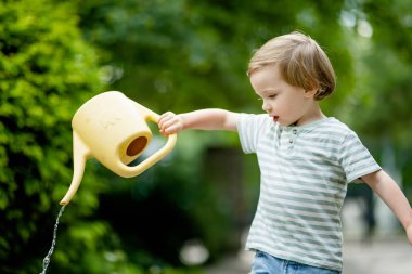 Yaz günü arka bahçede çiçek tarlalarını sulayan tatlı bir çocuk. Çocuk bitkileri sulamak için teneke kullanıyor. Çocuk günlük ev işlerine yardım ediyor. Annesinin küçük yardımcısı..