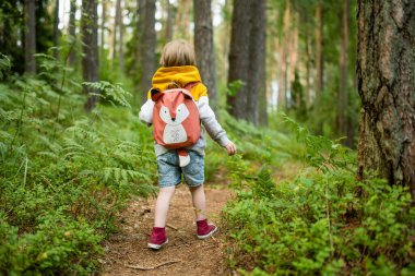 Sırt çantalı şirin bir çocuk güneşli bir yaz gününde dışarıda eğleniyor. Doğayı keşfeden çocuk. Çocuk seyahate çıkıyor. Çocuklu aileler için yaz etkinlikleri.