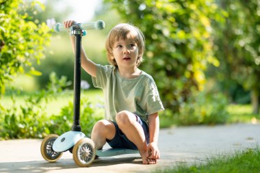 Güneşli bir yaz akşamında arka bahçede scooterını süren sevimli küçük bir çocuk. Paten süren küçük bir çocuk. Çocuklar için aktif eğlence ve açık hava sporları.