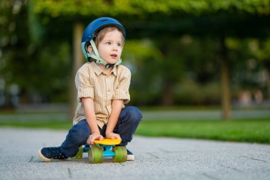 Güzel bir yaz gününde parkta kaykay öğrenen tatlı bir çocuk. Güvenlik kaskı takan çocuk dışarıda kaykay sürmekten zevk alıyor. Küçük çocuklar için aktif eğlence.