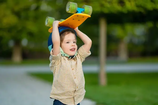 可爱的小男孩在一个美丽的夏天在公园里学习滑板 孩子们戴着安全帽 享受户外滑板之旅 幼儿的积极闲暇 图库图片