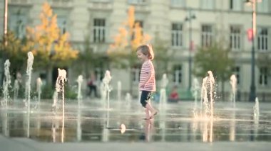 Küçük şirin çocuk şehir çeşmesinde suyla eğleniyor. Çocuk sıcak bir günde dışarıda su oyunu oynuyor. Küçük çocuklar için kentsel yaz aktiviteleri. Yavaş çekim görüntüleri.