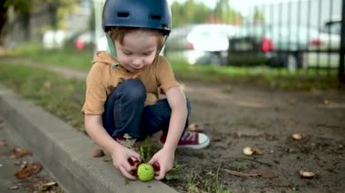 Sonbahar günü parkta kestane toplayan küçük bir çocuğun yakın çekimi. Çocuk kestane ve yaprakları ararken eğleniyor. Çocuklarla sonbahar aktiviteleri.