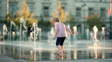 Küçük şirin çocuk şehir çeşmesinde suyla eğleniyor. Çocuk sıcak bir günde dışarıda su oyunu oynuyor. Küçük çocuklar için kentsel yaz aktiviteleri. Yavaş çekim görüntüleri.