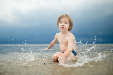 Sıcak ve güneşli bir yaz gününde kumlu bir plajda eğlenen sevimli küçük çocuk. Okyanus kenarında oynayan bir çocuk. Çocuklar için yaz etkinlikleri.