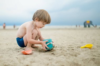 Sıcak ve güneşli bir yaz gününde kumlu bir plajda eğlenen sevimli küçük çocuk. Okyanus kenarında oynayan bir çocuk. Çocuklar için yaz etkinlikleri.