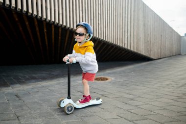 Tallinn limanında küçük şirin bir çocuk scooter kullanıyor. Küçük çocuklar için aktif eğlence.