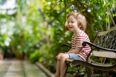 Estonya 'nın Tartu kentindeki botanik bahçesinde farklı tropikal bitki ve çiçek türlerini keşfeden küçük bir çocuk. Serada yetişen yemyeşil egzotik bitkiler..