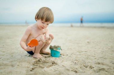 Sıcak ve güneşli bir yaz gününde kumlu bir plajda eğlenen sevimli küçük çocuk. Okyanus kenarında oynayan bir çocuk. Çocuklar için yaz etkinlikleri.