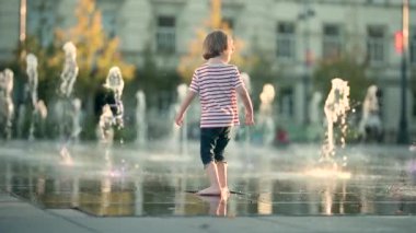 Küçük şirin çocuk şehir çeşmesinde suyla eğleniyor. Çocuk sıcak bir günde dışarıda su oyunu oynuyor. Küçük çocuklar için kentsel yaz aktiviteleri. Yavaş çekim görüntüleri.