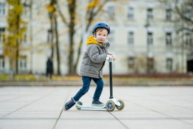 Sonbahar günü bir şehirde motosikletine binen sevimli küçük bir çocuk. Paten süren küçük bir çocuk. Çocuklar için aktif eğlence ve açık hava sporları.