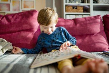 Parlak, güneşli bir öğleden sonra evdeki kanepede kitap okuyan sevimli küçük bir çocuk. Gündüz kreşinde yaratıcı aktivite. Çocuklar eğleniyor. Eğitici öğrenme oyunları.