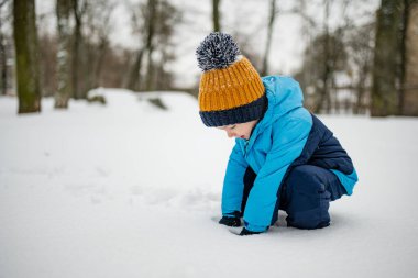 Tatlı çocuk, karlı bir kış gününde şehirde eğleniyor. Karda oynayan, kalın giysiler giymiş şirin bir çocuk. Çocuklu aileler için kış etkinlikleri.