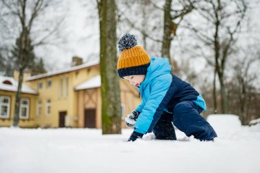 Tatlı çocuk, karlı bir kış gününde şehirde eğleniyor. Karda oynayan, kalın giysiler giymiş şirin bir çocuk. Çocuklu aileler için kış etkinlikleri.