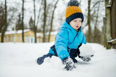 Tatlı çocuk, karlı bir kış gününde şehirde eğleniyor. Karda oynayan, kalın giysiler giymiş şirin bir çocuk. Çocuklu aileler için kış etkinlikleri.