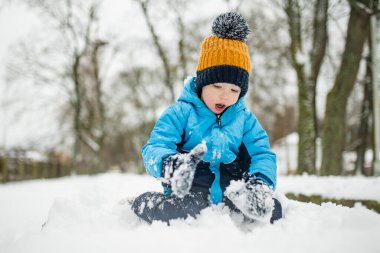Tatlı çocuk, karlı bir kış gününde şehirde eğleniyor. Karda oynayan, kalın giysiler giymiş şirin bir çocuk. Çocuklu aileler için kış etkinlikleri.
