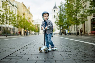 Güneşli bir sonbahar akşamında küçük sevimli bir çocuk mobiletini güneşli bir şehirde sürüyor. Paten süren küçük bir çocuk. Çocuklar için aktif eğlence ve açık hava sporları.