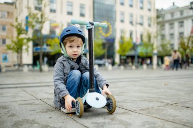 Güneşli bir sonbahar akşamında küçük sevimli bir çocuk mobiletini güneşli bir şehirde sürüyor. Paten süren küçük bir çocuk. Çocuklar için aktif eğlence ve açık hava sporları.