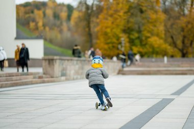 Sonbahar günü bir şehirde motosikletine binen sevimli küçük bir çocuk. Paten süren küçük bir çocuk. Çocuklar için aktif eğlence ve açık hava sporları.