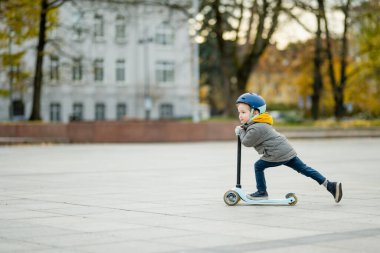 Sonbahar günü bir şehirde motosikletine binen sevimli küçük bir çocuk. Paten süren küçük bir çocuk. Çocuklar için aktif eğlence ve açık hava sporları.