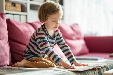Parlak, güneşli bir öğleden sonra evdeki kanepede kitap okuyan sevimli küçük bir çocuk. Gündüz kreşinde yaratıcı aktivite. Çocuklar eğleniyor. Eğitici öğrenme oyunları.
