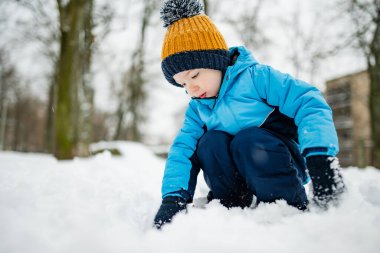 Tatlı çocuk, karlı bir kış gününde şehirde eğleniyor. Karda oynayan, kalın giysiler giymiş şirin bir çocuk. Çocuklu aileler için kış etkinlikleri.