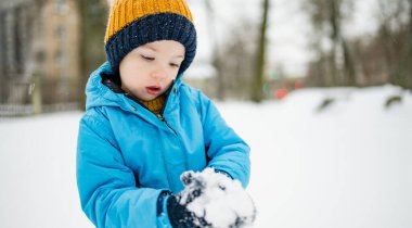 Tatlı çocuk, karlı bir kış gününde şehirde eğleniyor. Karda oynayan, kalın giysiler giymiş şirin bir çocuk. Çocuklu aileler için kış etkinlikleri.