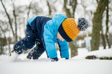 Tatlı çocuk, karlı bir kış gününde şehirde eğleniyor. Karda oynayan, kalın giysiler giymiş şirin bir çocuk. Çocuklu aileler için kış etkinlikleri.