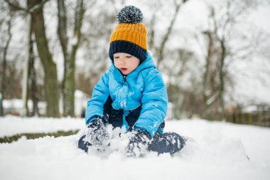 Tatlı çocuk, karlı bir kış gününde şehirde eğleniyor. Karda oynayan, kalın giysiler giymiş şirin bir çocuk. Çocuklu aileler için kış etkinlikleri.