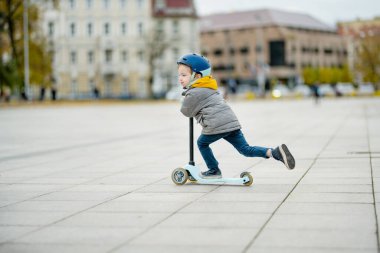 Sonbahar günü bir şehirde motosikletine binen sevimli küçük bir çocuk. Paten süren küçük bir çocuk. Çocuklar için aktif eğlence ve açık hava sporları.