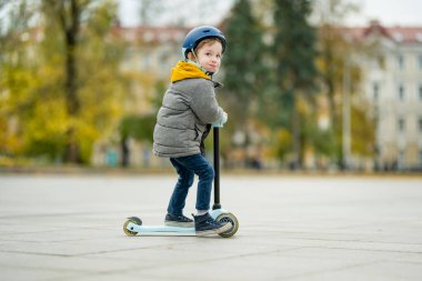 Sonbahar günü bir şehirde motosikletine binen sevimli küçük bir çocuk. Paten süren küçük bir çocuk. Çocuklar için aktif eğlence ve açık hava sporları.