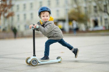 Sonbahar günü bir şehirde motosikletine binen sevimli küçük bir çocuk. Paten süren küçük bir çocuk. Çocuklar için aktif eğlence ve açık hava sporları.
