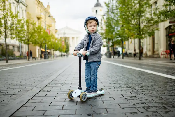 Güneşli bir sonbahar akşamında küçük sevimli bir çocuk mobiletini güneşli bir şehirde sürüyor. Paten süren küçük bir çocuk. Çocuklar için aktif eğlence ve açık hava sporları.