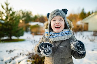 Sevimli küçük çocuk karlı kış gününde eğleniyor. Karda oynayan, kalın giysiler giymiş şirin bir çocuk. Çocuklu aileler için kış etkinlikleri.
