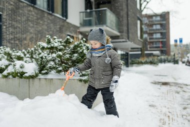 Karlı bir kış gününde küçük sevimli bir çocuk şehirde eğleniyor. Karda oynayan, kalın giysiler giymiş şirin bir çocuk. Çocuklu aileler için kış etkinlikleri.