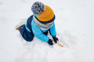 Sevimli küçük çocuk karlı kış gününde eğleniyor. Karda oynayan, kalın giysiler giymiş şirin bir çocuk. Çocuklu aileler için kış etkinlikleri.