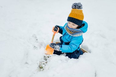 Sevimli küçük çocuk karlı kış gününde eğleniyor. Karda oynayan, kalın giysiler giymiş şirin bir çocuk. Çocuklu aileler için kış etkinlikleri.